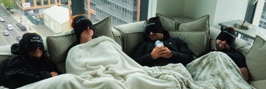 Four people laying on a couch wearing hangover hats.